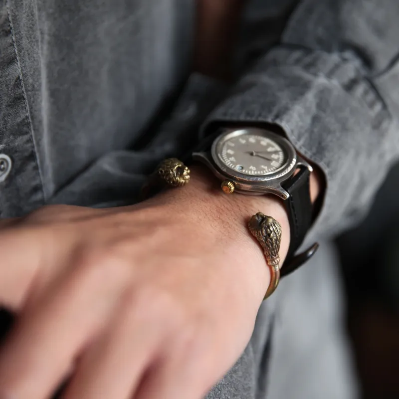 機械式時計と獅子のバングル。時計と重ねて身に着けてもリューズに当たらないデザインで、シルバーと真鍮の異素材が好相性。